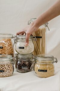 A hand organizing labeled glass jars filled with dry goods like pasta and grains, representing organized zero-waste kitchen storage.